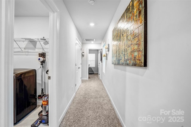 hallway featuring baseboards, washer / dryer, visible vents, and light colored carpet