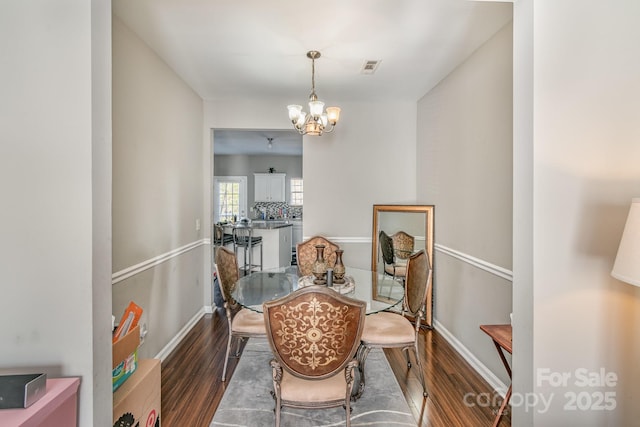 dining space with dark wood-type flooring, a chandelier, and baseboards