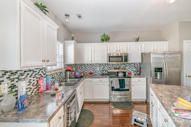 kitchen featuring tasteful backsplash, white cabinets, appliances with stainless steel finishes, dark wood-style flooring, and a sink