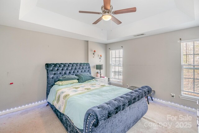 bedroom featuring a raised ceiling, light carpet, visible vents, and baseboards