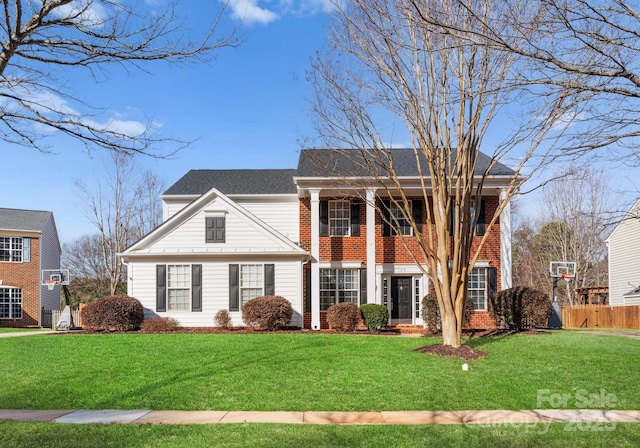 neoclassical / greek revival house with brick siding, a front yard, and fence