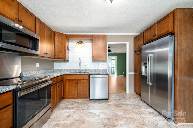 kitchen featuring brown cabinetry, a sink, ceiling fan, and stainless steel appliances