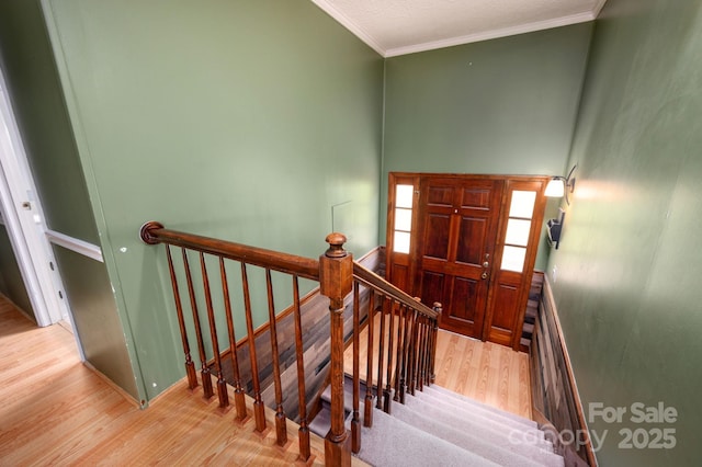 stairs with wood finished floors, ornamental molding, and baseboards