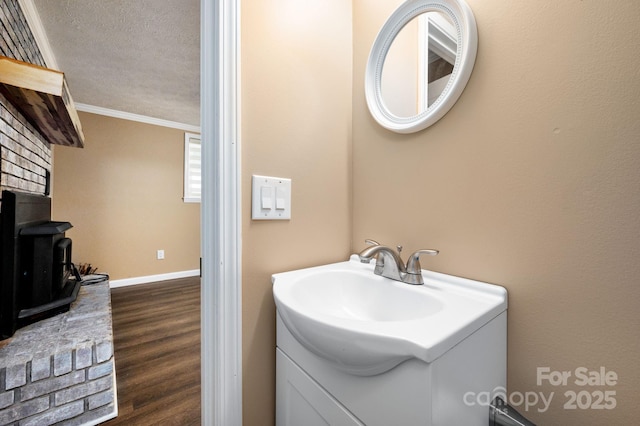 bathroom with a wood stove, vanity, crown molding, baseboards, and wood finished floors