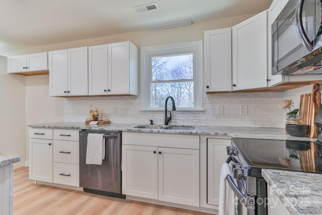 kitchen featuring stainless steel appliances, a sink, visible vents, white cabinets, and light stone countertops