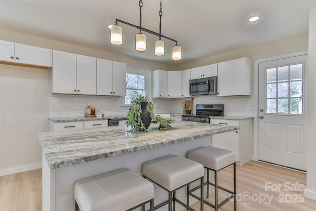 kitchen featuring appliances with stainless steel finishes, a breakfast bar area, hanging light fixtures, light wood-type flooring, and white cabinetry