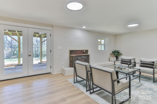 interior space with brick wall, light wood-style flooring, a fireplace, and french doors