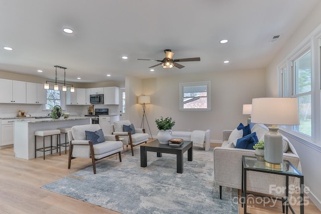 living room with light wood-style flooring, visible vents, a wealth of natural light, and recessed lighting