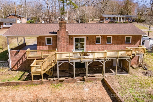 back of property featuring brick siding, roof with shingles, a chimney, stairway, and a wooden deck