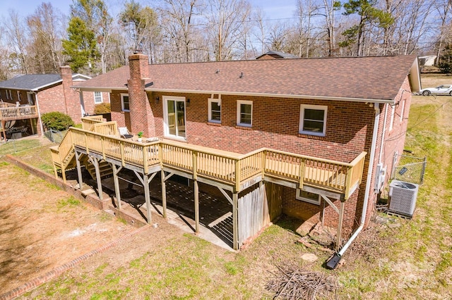 rear view of house with central air condition unit, brick siding, a shingled roof, a wooden deck, and a chimney