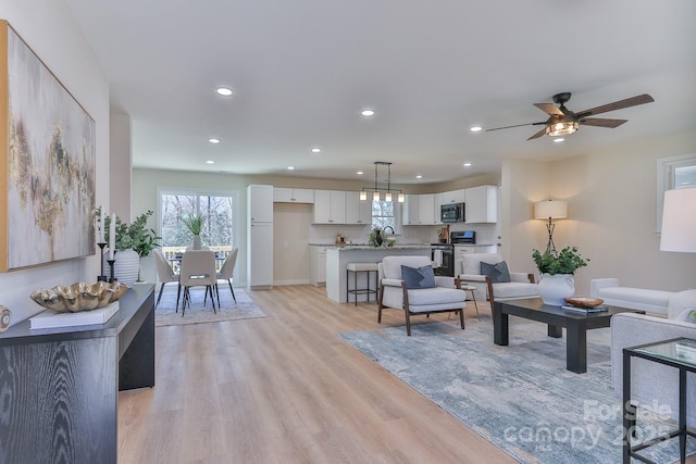 living room with light wood finished floors, a ceiling fan, and recessed lighting