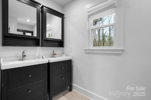 bathroom with baseboards, a sink, and two vanities