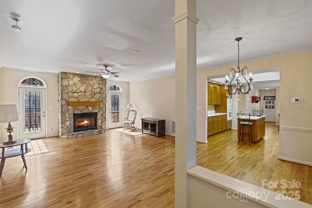 living room with light wood-type flooring, a stone fireplace, ornate columns, ceiling fan, and crown molding