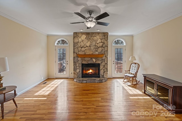 living room featuring light wood-type flooring, ceiling fan, a stone fireplace, and ornamental molding