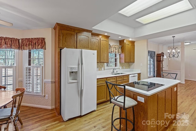 kitchen with white appliances, light wood-type flooring, decorative light fixtures, a center island, and sink