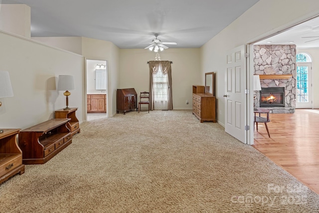 living area with light carpet, ceiling fan, and a stone fireplace