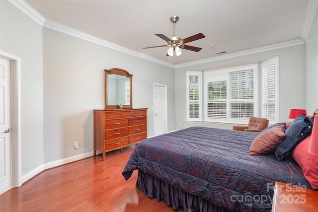 bedroom with baseboards, wood finished floors, visible vents, and crown molding