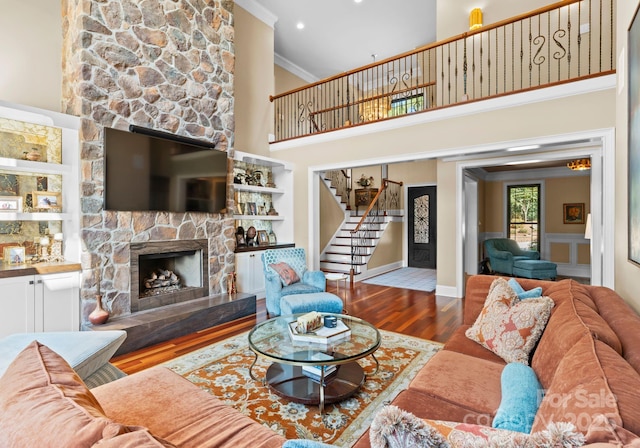 living room featuring ornamental molding, a stone fireplace, a high ceiling, and wood-type flooring