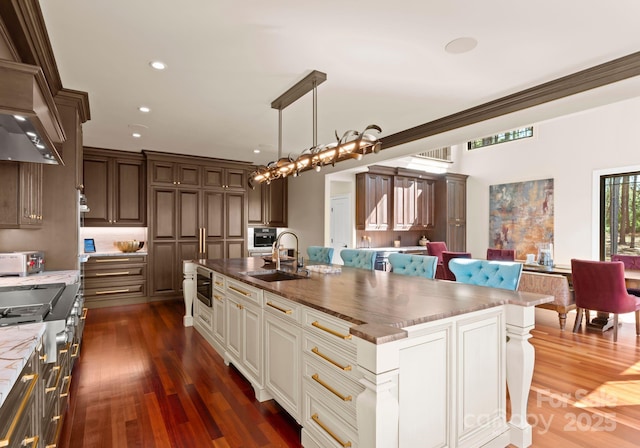 kitchen with dark wood-type flooring, stainless steel appliances, decorative light fixtures, a spacious island, and sink