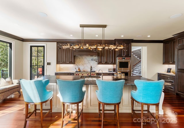 kitchen featuring dark brown cabinetry, an island with sink, double oven, and dark hardwood / wood-style floors