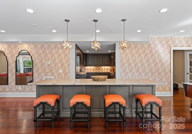 kitchen with light stone countertops, a kitchen breakfast bar, dark wood-type flooring, and decorative light fixtures