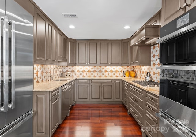 kitchen featuring appliances with stainless steel finishes, sink, light stone counters, dark hardwood / wood-style flooring, and tasteful backsplash