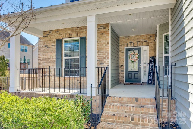 view of exterior entry with brick siding and a porch