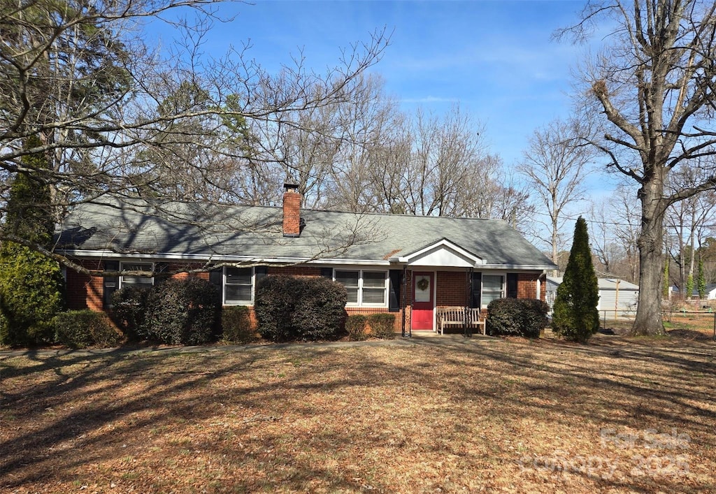 view of front of house featuring a front yard, a chimney, a porch, and brick siding