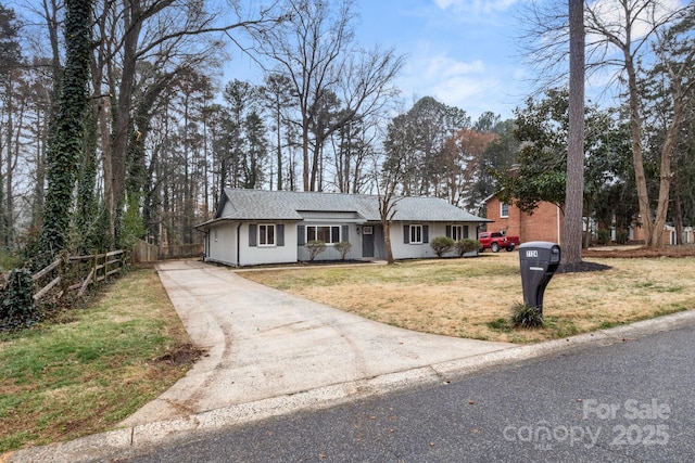 ranch-style home featuring roof with shingles, fence, a front lawn, and driveway