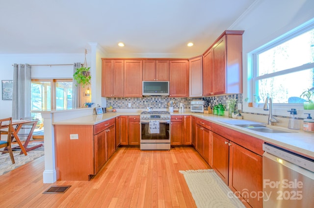 kitchen with stainless steel appliances, a peninsula, a sink, visible vents, and crown molding