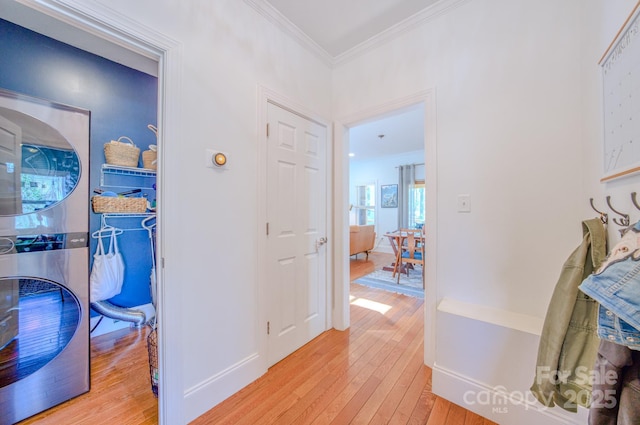 corridor featuring crown molding, stacked washing maching and dryer, baseboards, and light wood-style floors