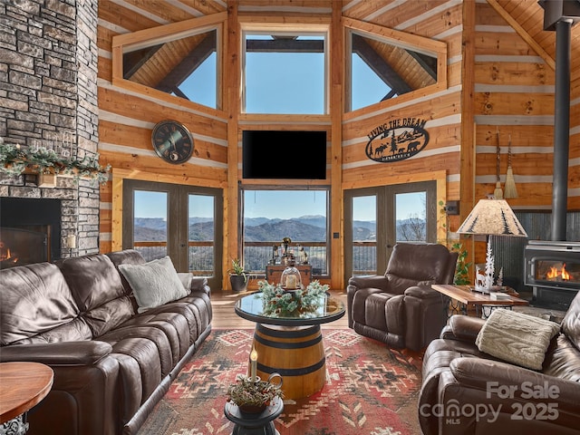 living room with french doors, wood finished floors, a wood stove, a stone fireplace, and wood walls