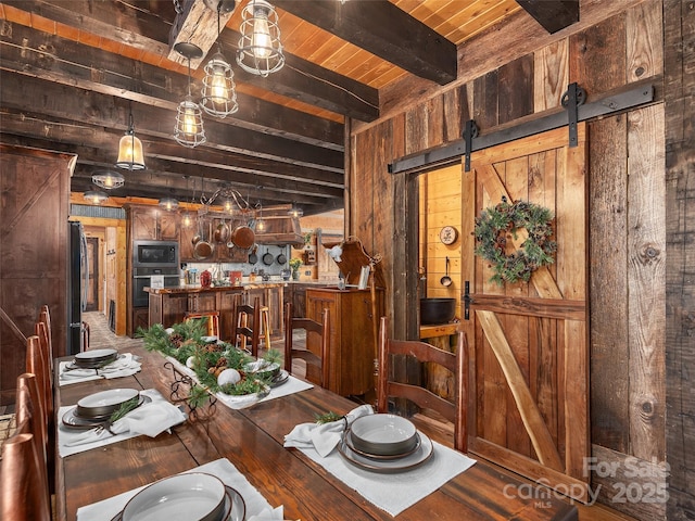 dining room featuring wooden ceiling, a barn door, wooden walls, and beamed ceiling