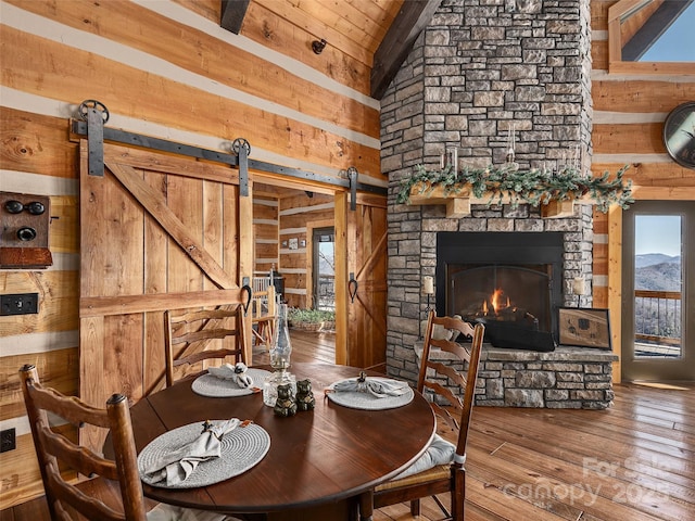 dining area with wood walls, a barn door, wood-type flooring, and a stone fireplace