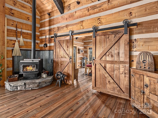 living room with a wood stove, a barn door, wooden walls, and wood-type flooring