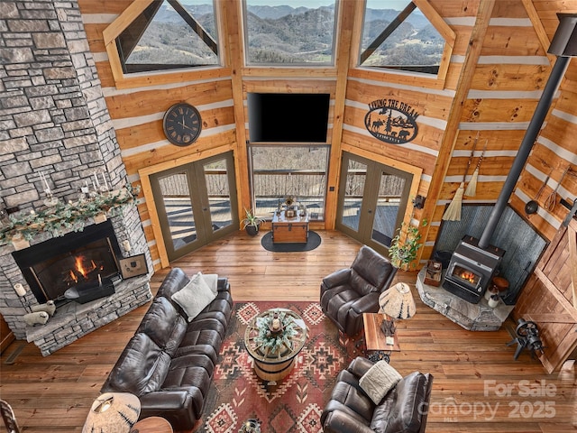 living area with a stone fireplace, a high ceiling, french doors, wood-type flooring, and a wood stove