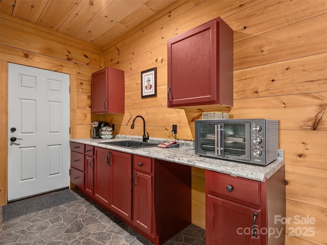 kitchen with reddish brown cabinets, wood ceiling, wooden walls, and a sink