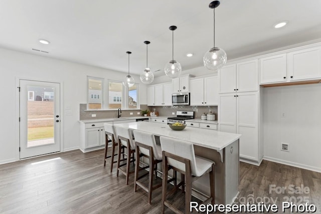 kitchen with a center island, white cabinets, pendant lighting, stainless steel appliances, and backsplash