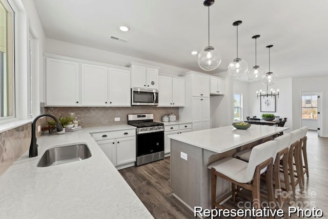 kitchen with sink, white cabinetry, stainless steel appliances, a kitchen island, and decorative light fixtures