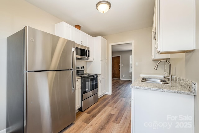 kitchen featuring appliances with stainless steel finishes, light hardwood / wood-style flooring, light stone counters, sink, and white cabinetry