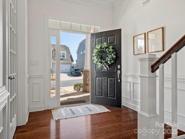 foyer with dark wood finished floors, stairway, a wainscoted wall, ornamental molding, and a decorative wall