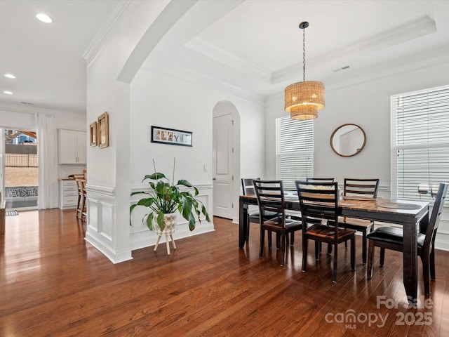 dining area with dark wood finished floors, a tray ceiling, a decorative wall, and arched walkways