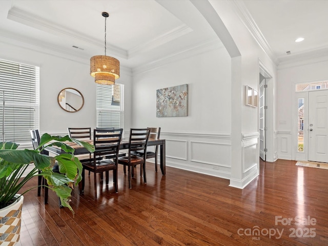 dining area featuring arched walkways, a decorative wall, a raised ceiling, and wood finished floors