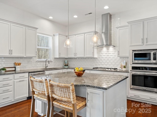 kitchen featuring visible vents, a center island, wall chimney range hood, appliances with stainless steel finishes, and a sink