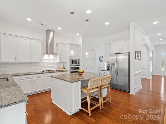 kitchen with dark wood-type flooring, backsplash, arched walkways, appliances with stainless steel finishes, and wall chimney exhaust hood