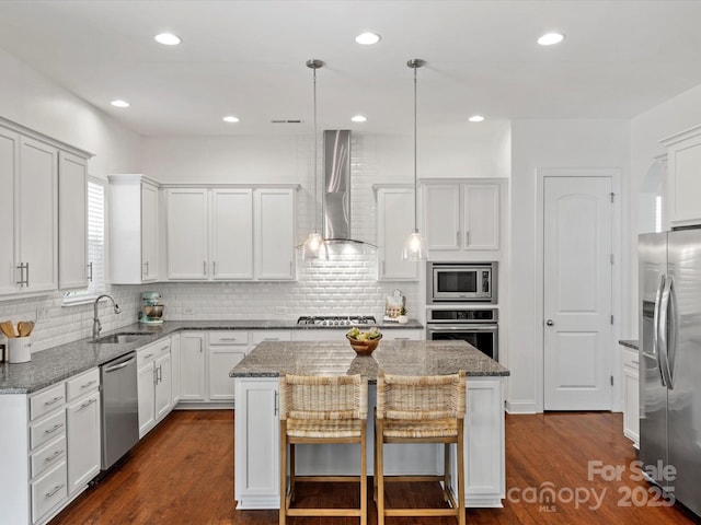 kitchen with a kitchen island, a sink, stainless steel appliances, dark wood-type flooring, and wall chimney exhaust hood