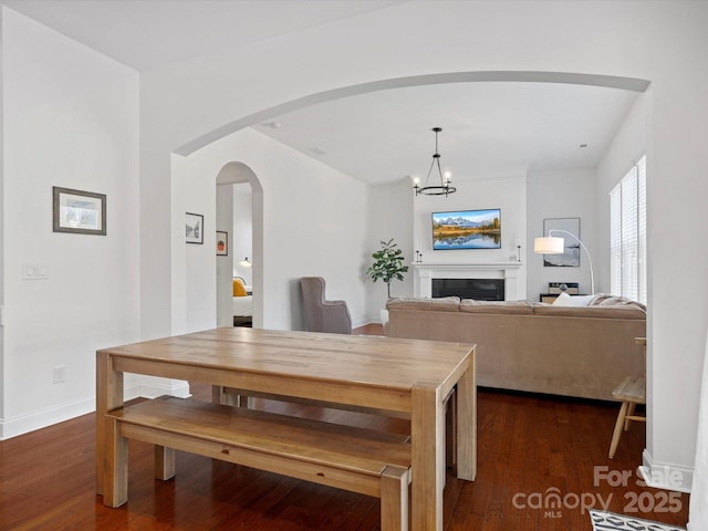 dining room featuring dark wood finished floors, arched walkways, an inviting chandelier, a fireplace, and baseboards