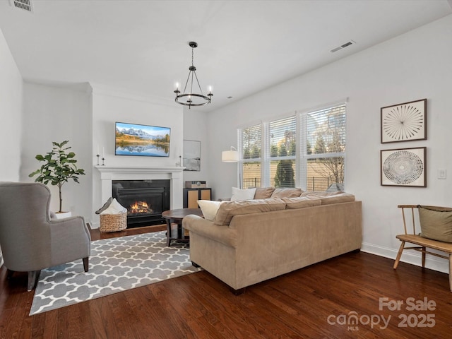 living room featuring a glass covered fireplace, dark wood-style floors, visible vents, and a chandelier