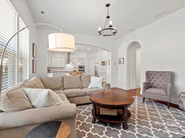 living area featuring arched walkways, a notable chandelier, visible vents, and wood finished floors