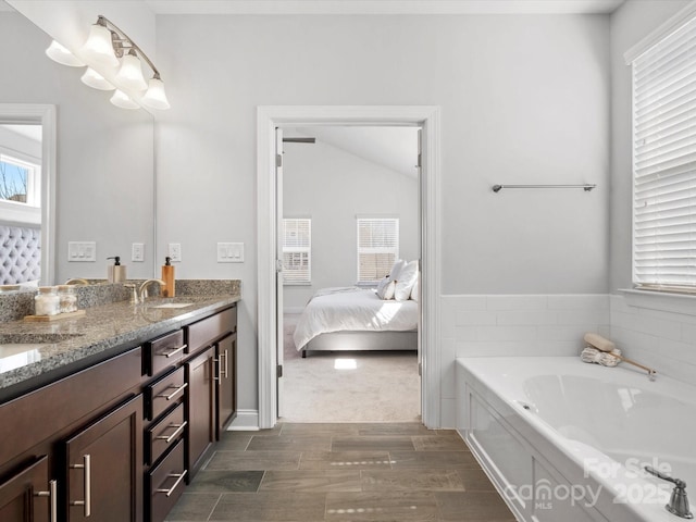 ensuite bathroom with connected bathroom, a garden tub, double vanity, wood finished floors, and a sink